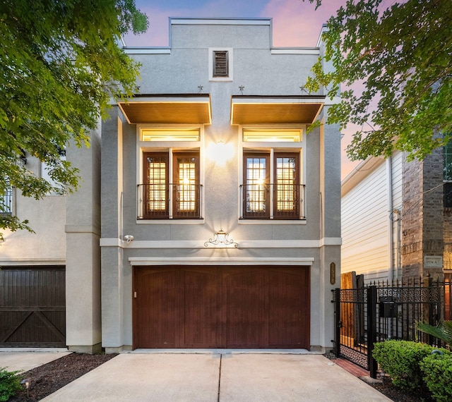 view of front of house with a garage, stucco siding, driveway, and fence