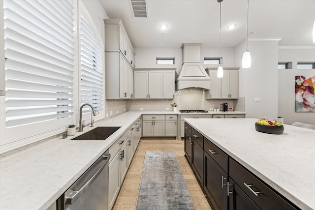 kitchen with backsplash, decorative light fixtures, stainless steel dishwasher, a sink, and premium range hood