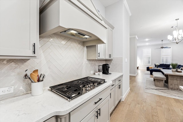 kitchen with light stone counters, stainless steel gas cooktop, white cabinetry, open floor plan, and backsplash