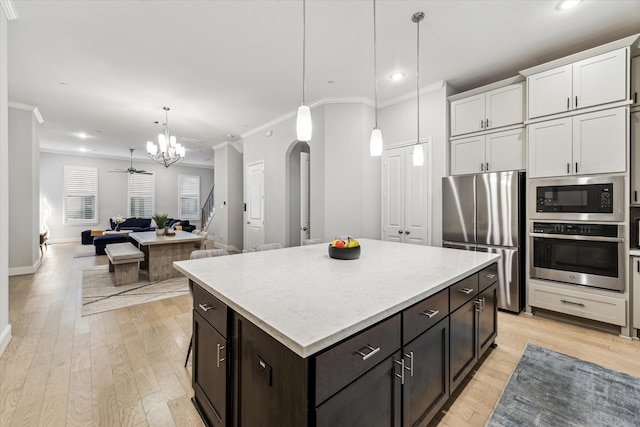 kitchen with white cabinets, appliances with stainless steel finishes, a chandelier, light wood-type flooring, and ornamental molding