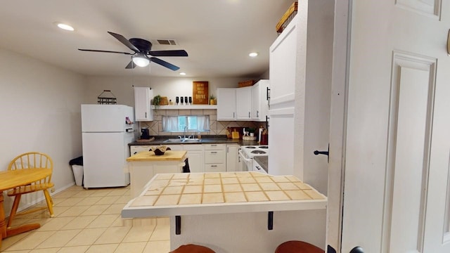 kitchen with a sink, tasteful backsplash, white appliances, and white cabinets