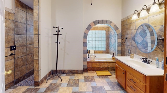 bathroom with walk in shower, vanity, baseboards, stone finish flooring, and a garden tub
