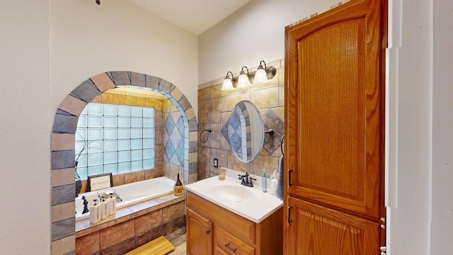 bathroom featuring a relaxing tiled tub, tile walls, and vanity