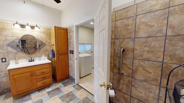 full bath with vanity, washer / dryer, tile walls, ceiling fan, and a tile shower