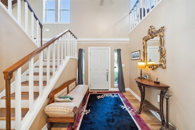 entryway with stairway, baseboards, a high ceiling, and wood finished floors
