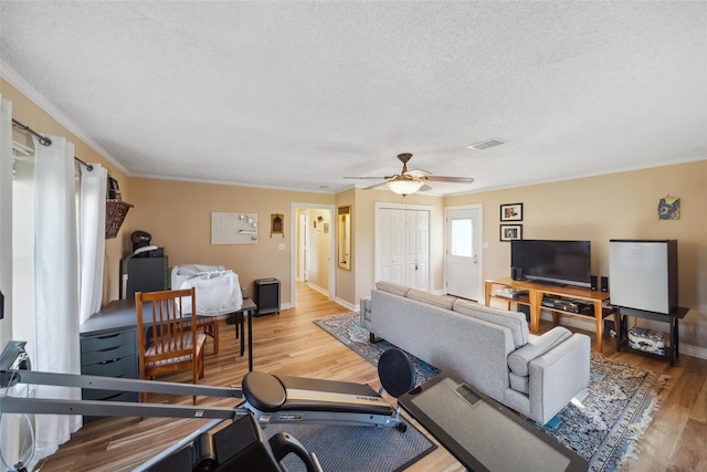 living room with a ceiling fan, visible vents, light wood-type flooring, baseboards, and ornamental molding