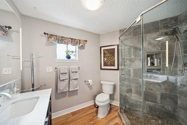bathroom with vanity, toilet, a textured ceiling, wood finished floors, and a stall shower