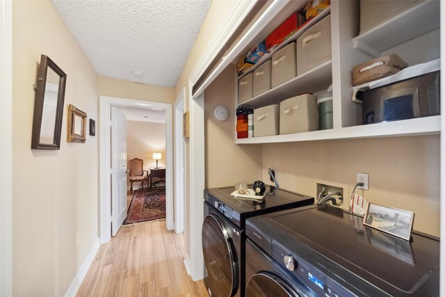 clothes washing area featuring laundry area, light wood finished floors, a textured ceiling, baseboards, and washer and clothes dryer