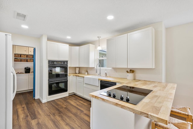 kitchen with a peninsula, dark wood-type flooring, white cabinetry, a sink, and black appliances