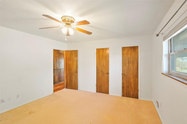 unfurnished bedroom featuring ceiling fan, a textured ceiling, baseboards, two closets, and carpet