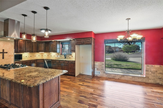 kitchen with wall chimney range hood, a textured ceiling, wood finished floors, an inviting chandelier, and stainless steel appliances