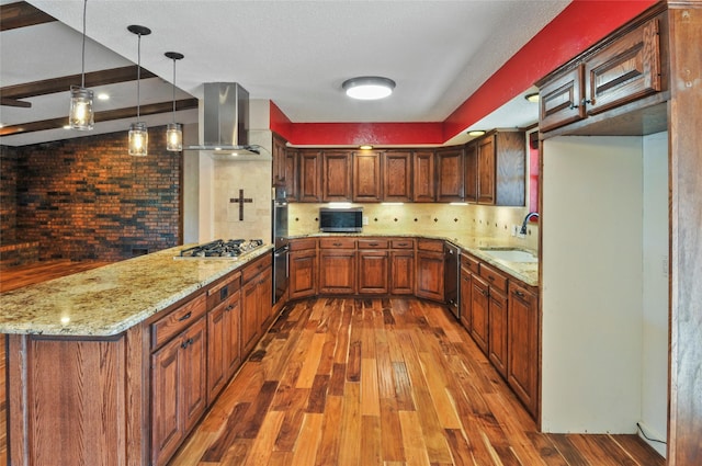 kitchen featuring wall chimney range hood, a sink, stainless steel appliances, a peninsula, and hardwood / wood-style flooring