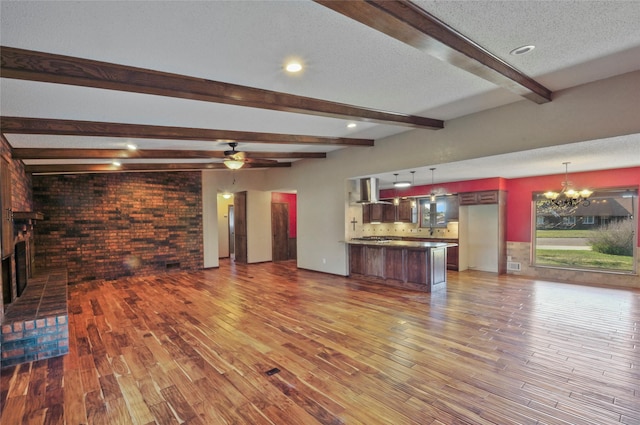 unfurnished living room featuring brick wall, visible vents, beam ceiling, wood finished floors, and ceiling fan with notable chandelier