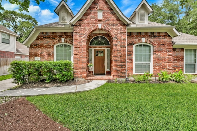 view of front facade with a shingled roof, brick siding, fence, and a front yard