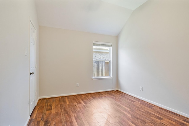 spare room with baseboards, vaulted ceiling, and wood finished floors