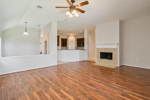 unfurnished living room with ceiling fan, visible vents, a tiled fireplace, dark wood finished floors, and baseboards