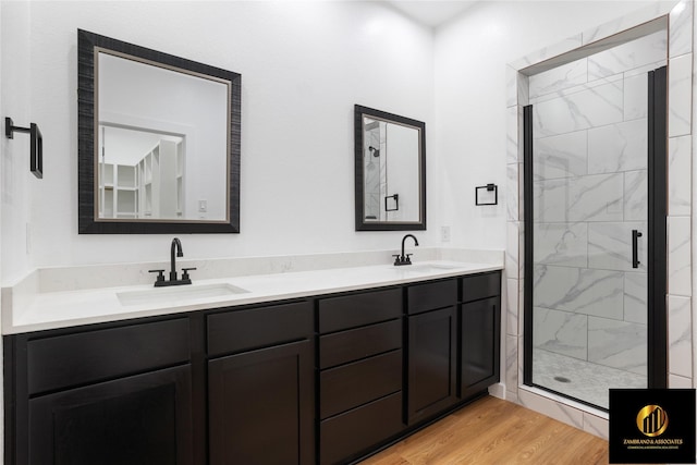full bath featuring wood finished floors, double vanity, a sink, and a stall shower