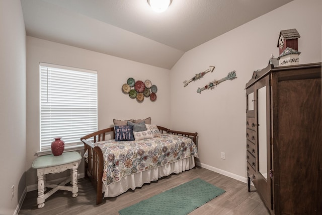 bedroom featuring baseboards, wood finished floors, and lofted ceiling