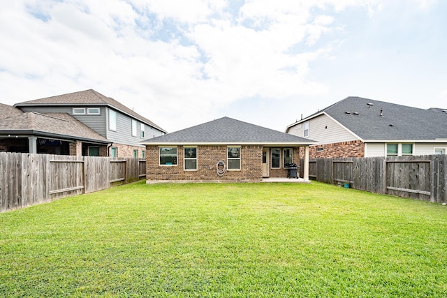 rear view of house with roof with shingles, brick siding, a fenced backyard, a yard, and a patio