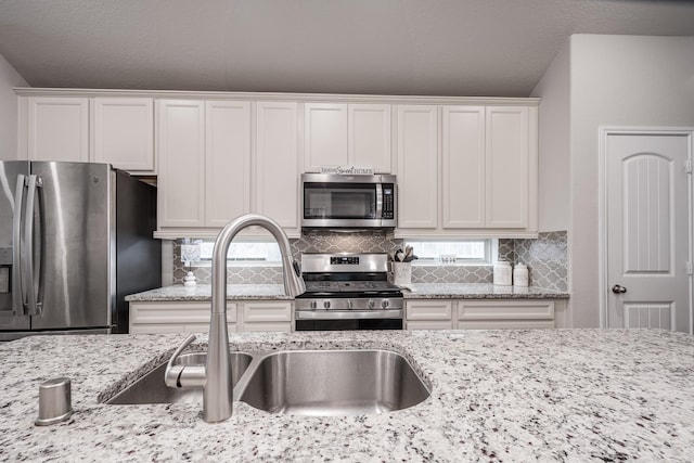 kitchen featuring light stone counters, a sink, stainless steel appliances, white cabinetry, and backsplash