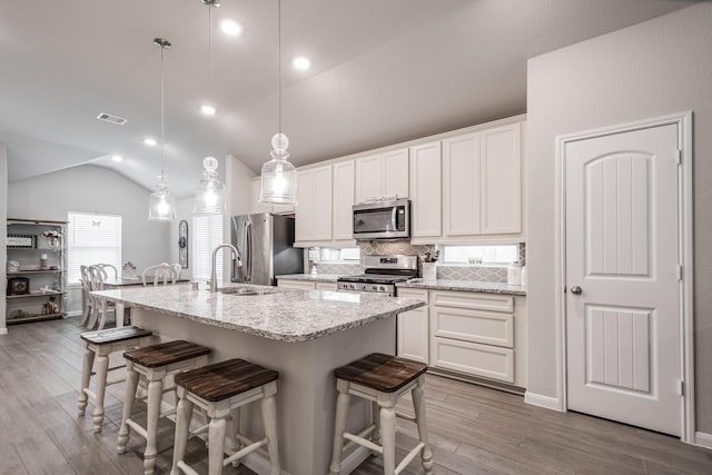 kitchen with a breakfast bar area, vaulted ceiling, wood finished floors, a sink, and stainless steel appliances