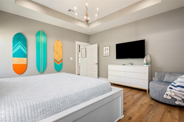 bedroom with wood-type flooring, a chandelier, a tray ceiling, and visible vents
