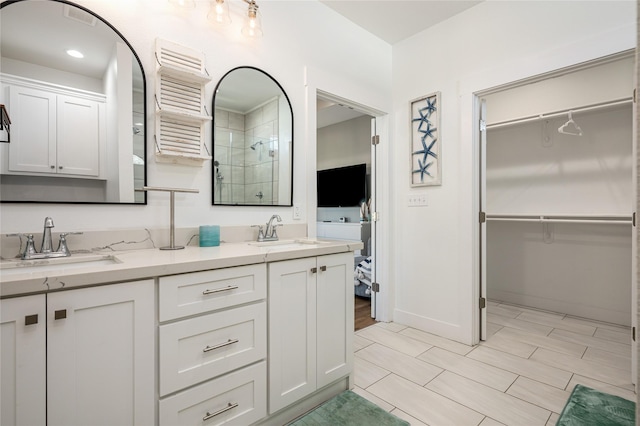bathroom with double vanity, a walk in closet, a sink, and a stall shower