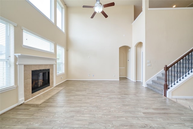 24618 Malca Manor Dr, Katy, TX 77493 - unfurnished living room featuring a high ceiling, arched walkways, a tiled fireplace, a ceiling fan, and wood finished floors