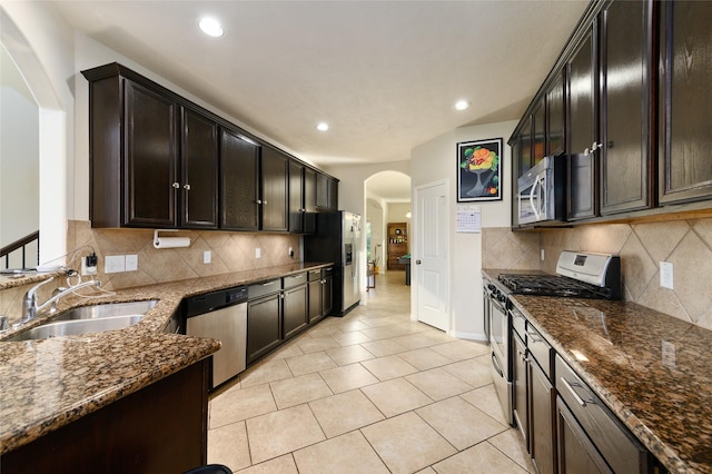 24618 Malca Manor Dr, Katy, TX 77493 - kitchen with appliances with stainless steel finishes, arched walkways, a sink, light tile patterned floors, and dark stone countertops