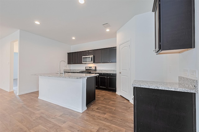 12518 Pelican Bay Dr, Houston, TX 77038 - kitchen with visible vents, appliances with stainless steel finishes, light stone countertops, light wood-style flooring, and an island with sink