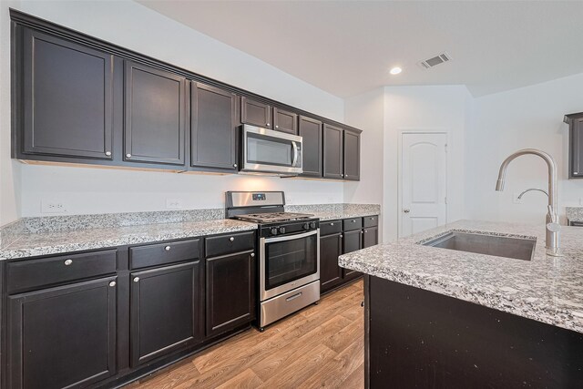 12518 Pelican Bay Dr, Houston, TX 77038 - kitchen featuring light stone countertops, a sink, light wood-style floors, stainless steel appliances, and visible vents