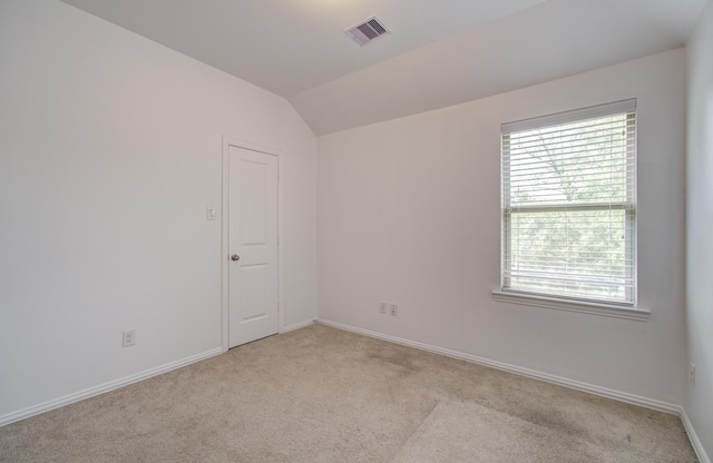 spare room featuring visible vents, baseboards, lofted ceiling, and light carpet