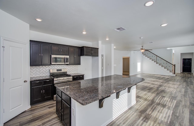 kitchen featuring appliances with stainless steel finishes, dark stone counters, wood finished floors, tasteful backsplash, and visible vents
