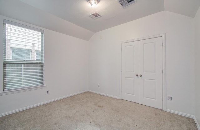 carpeted spare room featuring baseboards, visible vents, and lofted ceiling