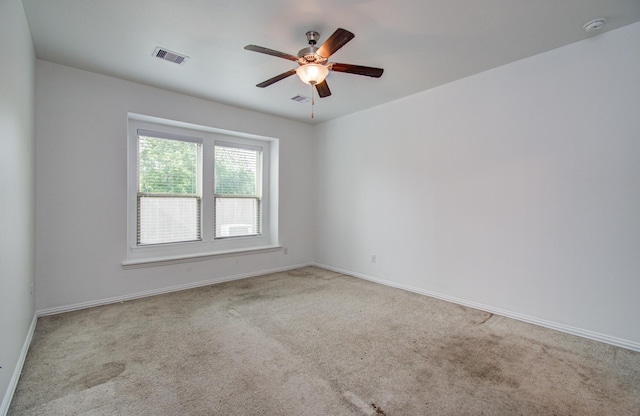 carpeted spare room with visible vents, baseboards, and ceiling fan