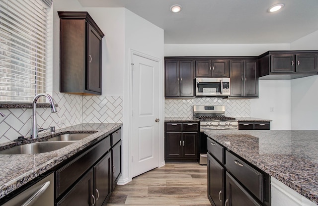 3730 Bach St, Iowa Colony, TX 77583 - kitchen featuring appliances with stainless steel finishes, dark stone countertops, tasteful backsplash, dark brown cabinets, and light wood-style flooring