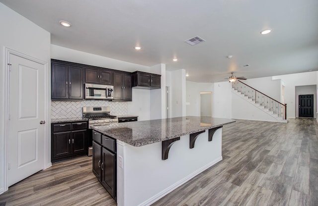 3730 Bach St, Iowa Colony, TX 77583 - kitchen featuring appliances with stainless steel finishes, wood finished floors, dark stone counters, a kitchen island, and a breakfast bar