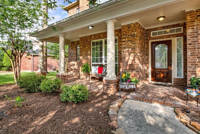 doorway to property featuring a porch and brick siding