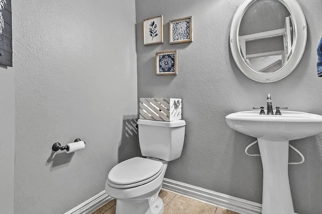 bathroom featuring toilet, baseboards, a sink, and tile patterned flooring