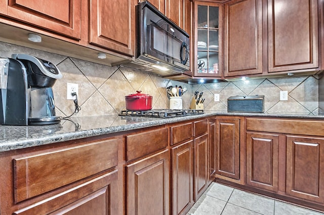 kitchen featuring brown cabinets, stone countertops, black microwave, and decorative backsplash
