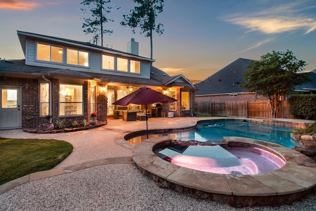 pool at dusk featuring a pool with connected hot tub, outdoor lounge area, a fenced backyard, and a patio area