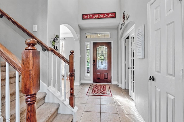 foyer with light tile patterned floors, arched walkways, a high ceiling, and stairs