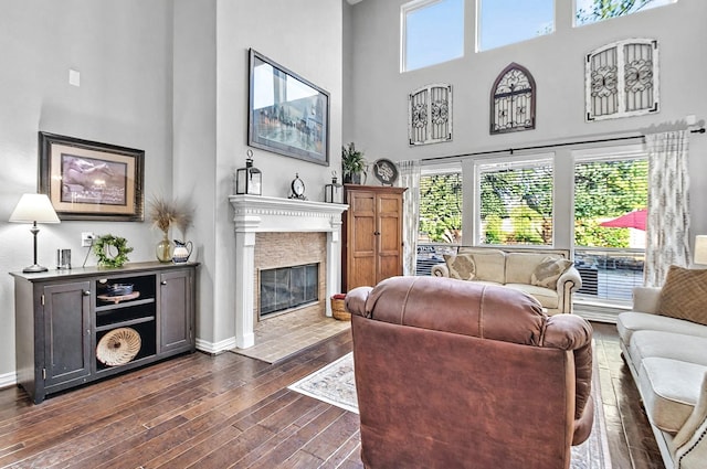 living area featuring dark wood-style flooring, a high ceiling, a fireplace with flush hearth, and baseboards