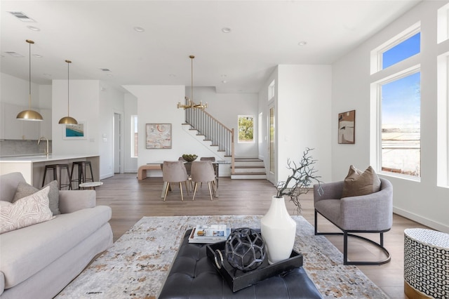 living room featuring an inviting chandelier, light wood finished floors, stairs, and visible vents