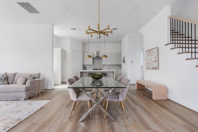 dining room featuring visible vents, light wood-type flooring, stairway, baseboards, and an inviting chandelier