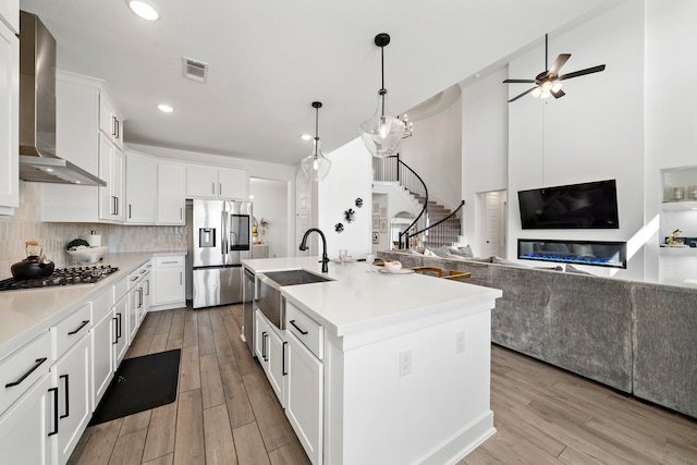 kitchen with visible vents, appliances with stainless steel finishes, a sink, open floor plan, and wall chimney exhaust hood