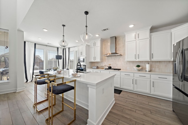 kitchen featuring light countertops, light wood-style flooring, wall chimney exhaust hood, and stainless steel appliances