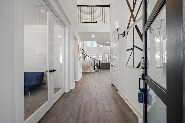 hall with french doors, a towering ceiling, dark wood finished floors, baseboards, and stairs