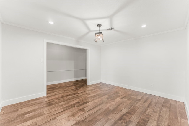 empty room featuring crown molding, baseboards, wood finished floors, and visible vents