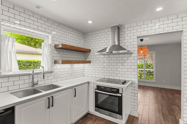 kitchen featuring oven, black electric stovetop, light countertops, wall chimney exhaust hood, and a sink